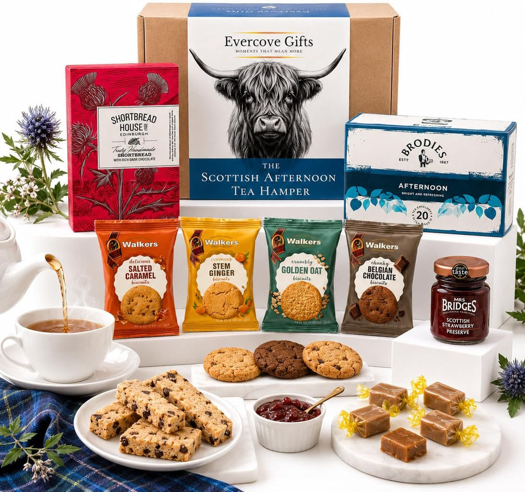 A curated tea and biscuit gift hamper arrangement on a white pedestal, featuring an Evercove Gifts box, a Bridgette Afternoon Tea box, several Walker's tea bags, a jar of Bridges preserves, cookies, scones, jam, and chocolate squares, with a teacup and floral props around it.